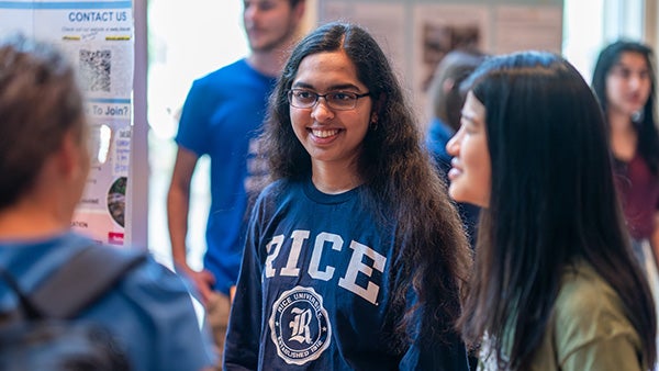 Three students speaking to one another, one with Rice University branded attire