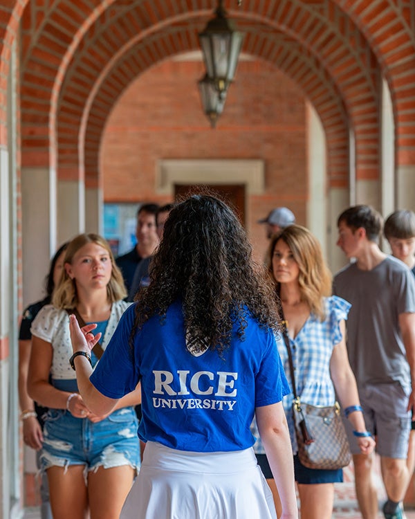 A person with their back facing the camera, wearing Rice University branded attire, a crowd of people facing the camera following them