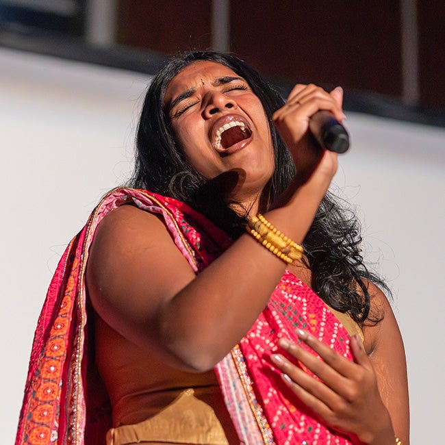Girl singing, holding a mic away from her face as she hits a high note