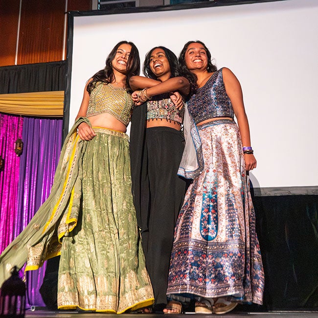 Three girls in Indian dresses leaning against one another, smiling
