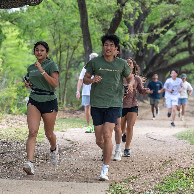Two people in matching green shirts and black shorts running through tree-covered path