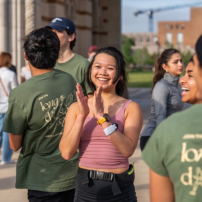 Girl in pink shirt clapping, people in green shirts standing around her