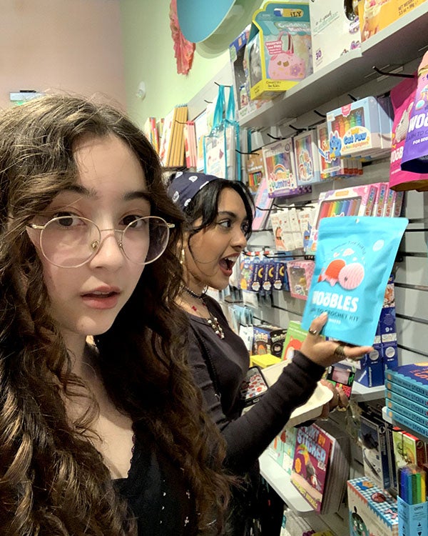 Girl taking photo of other girl pulling item from colorful shelves at a store