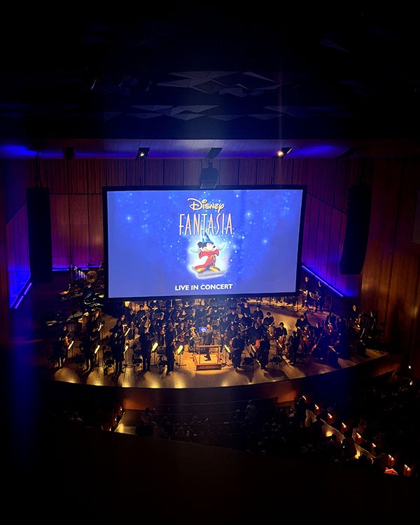 Far up shot of stage with orchestra performers and a large LED screen