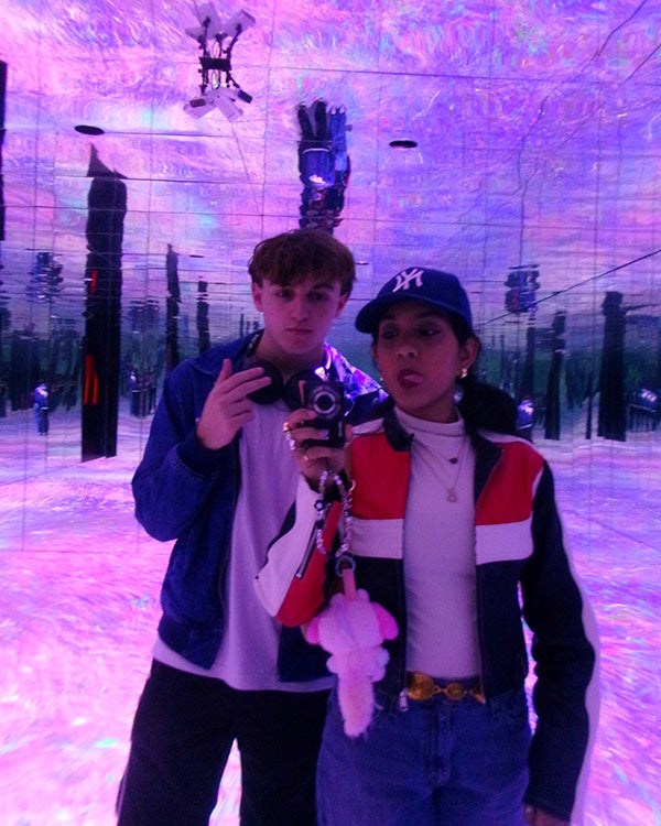 Mirror selfie of two people in a kaleidoscopic, purple lit room