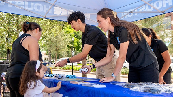 Two people handing out merch to a little child from behind a blue-cloth-covered table