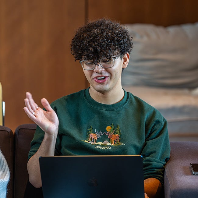A guy gesturing mid-speech, looking down at a computer