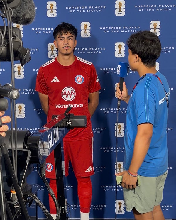 A man in an all-red uniform being interviewed by a guy in a blue shirt, with partially visible cameras pointed toward him