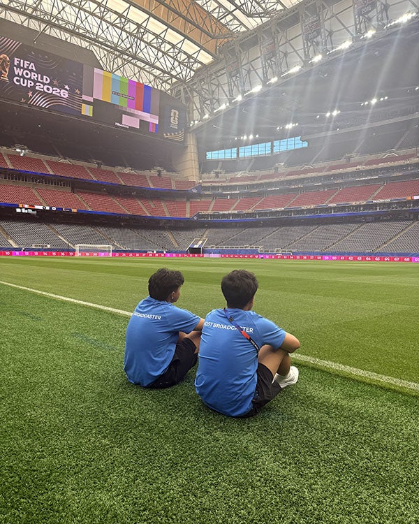 Two boys sitting on a soccer field with their backs to the camera