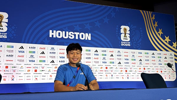 A guy sitting in a broadcasting booth, with several sponsor and FIFA World Cup logos behind him
