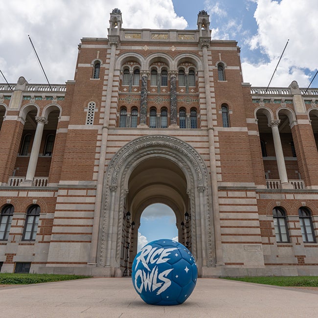 A blue soccer ball sitting on the pathway in front of the open archway of an old-architecture building