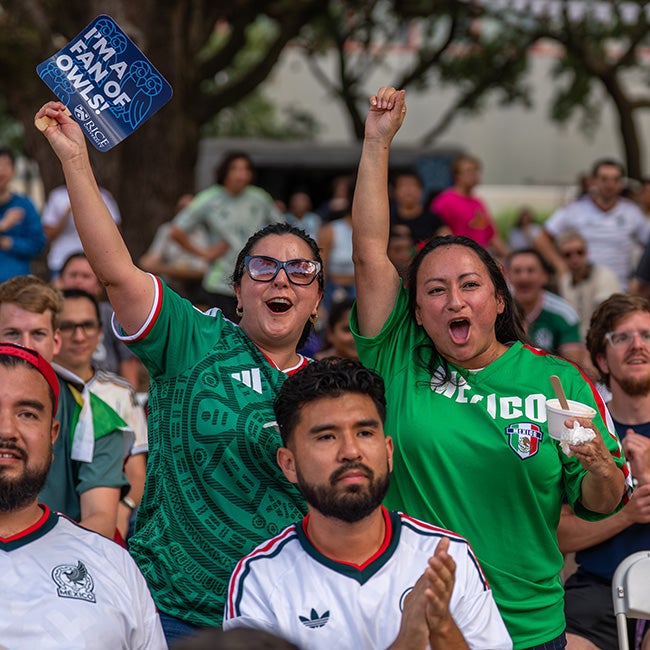 Two ladies in green jerseys standing with raised arms, mouths open mid-cheer