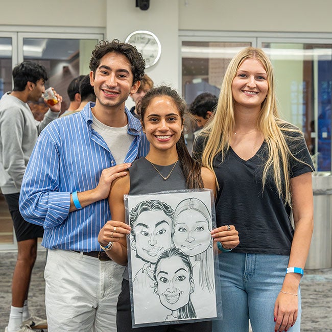 Three people standing together, holding a caricature sketch