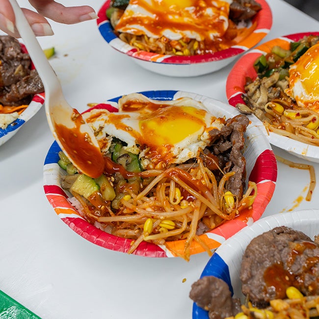 Several disposable bowls filled with food, including meat, vegetables, an egg, and sauce