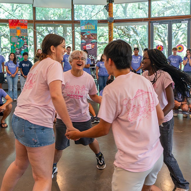 Four people in matching pink shirts, standing in a circle and holding hands