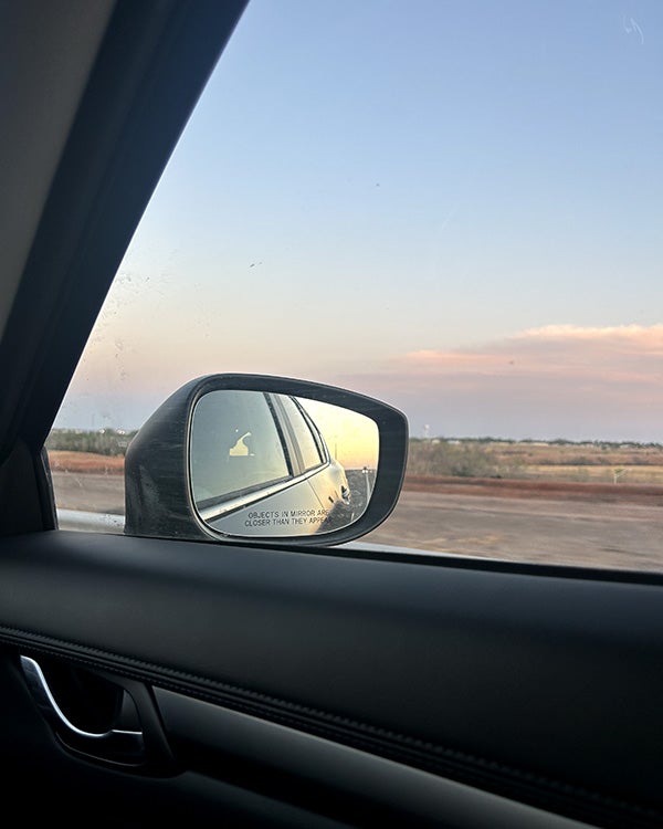 View out a car window of open prairie land, with the side mirror visible in the shot