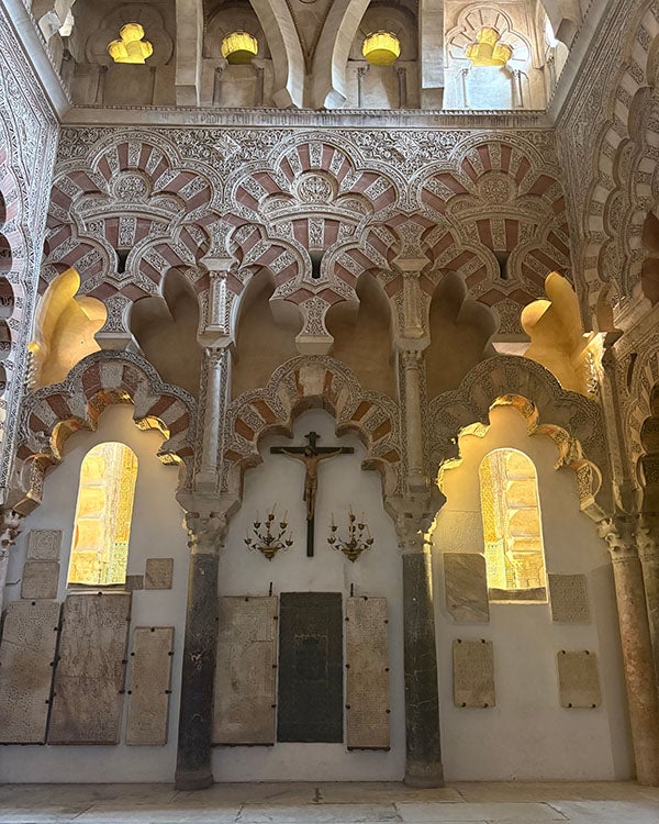 A cross on an ornately decorated and carved wall with doorways and balconies