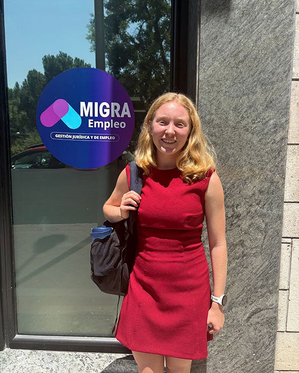a girl standing in front of a glass window with a logo for Migra Empleo on it