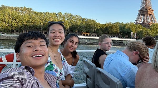 Selfie of students on a boat on a canal, passing by the Eiffel Tower