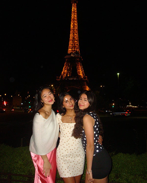 Three girls in front of the lit-up Eiffel Tower at night