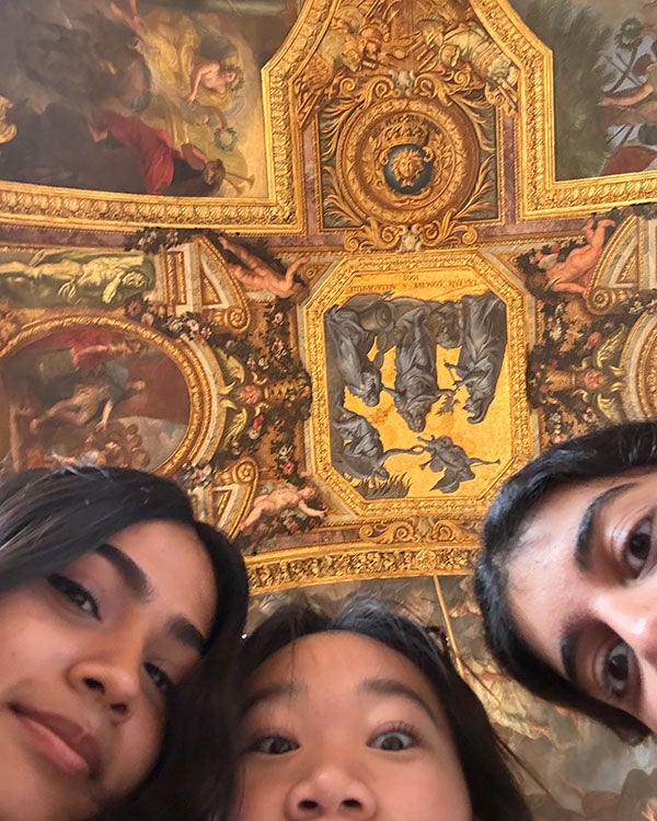 Three girls looking down at the camera, a vividly painted ceiling in the background