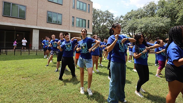 People standing in an array, mid-dance, in an outdoor courtyard