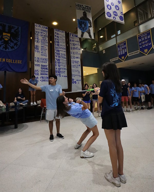 Two people holding up a limbo pole for a person bending to pass under it 