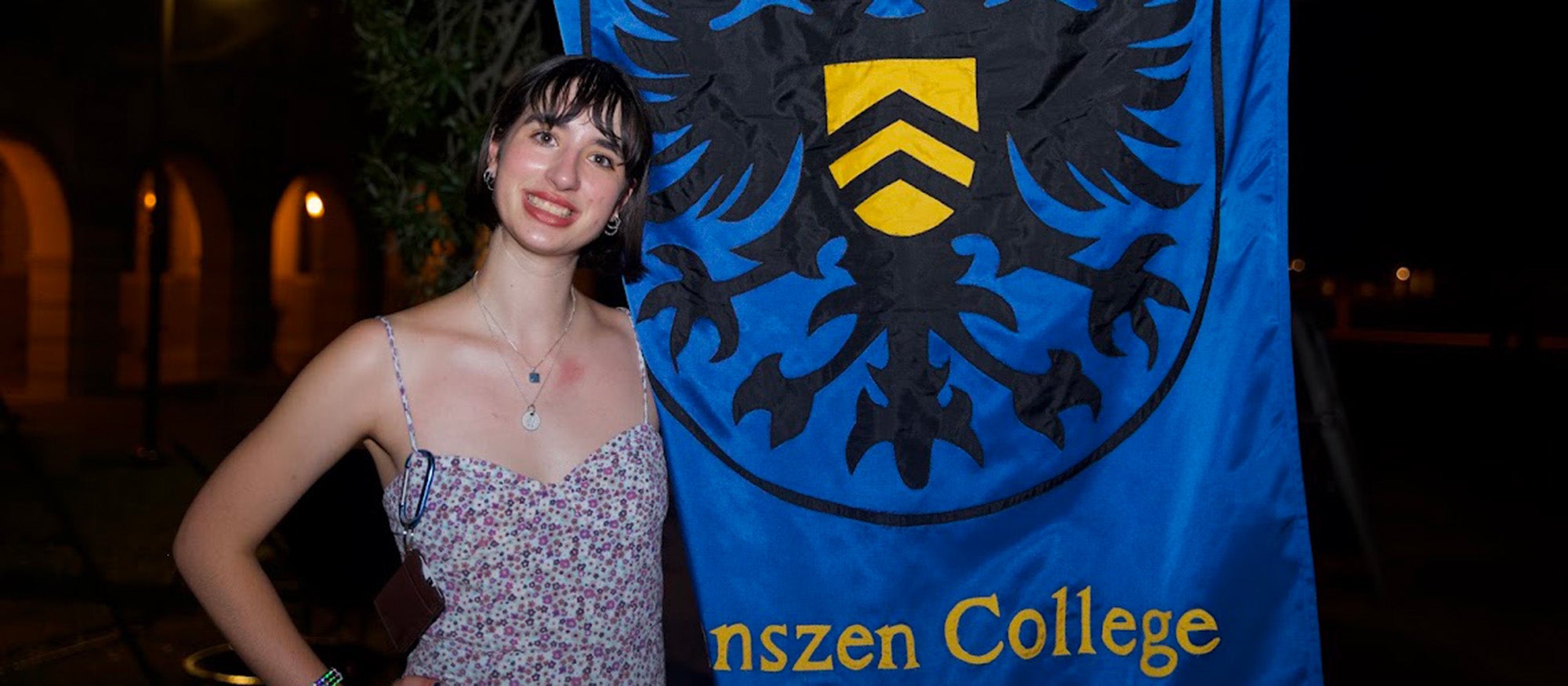 A girl smiling, standing next to a banner at nighttime