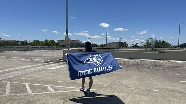 Girl in a parking lot, holding a flag behind her, turned so the flag faces the screen