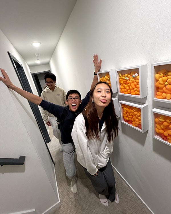 Fisheye image of three people walking in a hallway, the middle one having excited expression with his hands up 