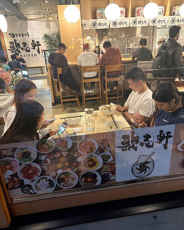 View from outside of four people sitting at a table inside an Japanese restaurant