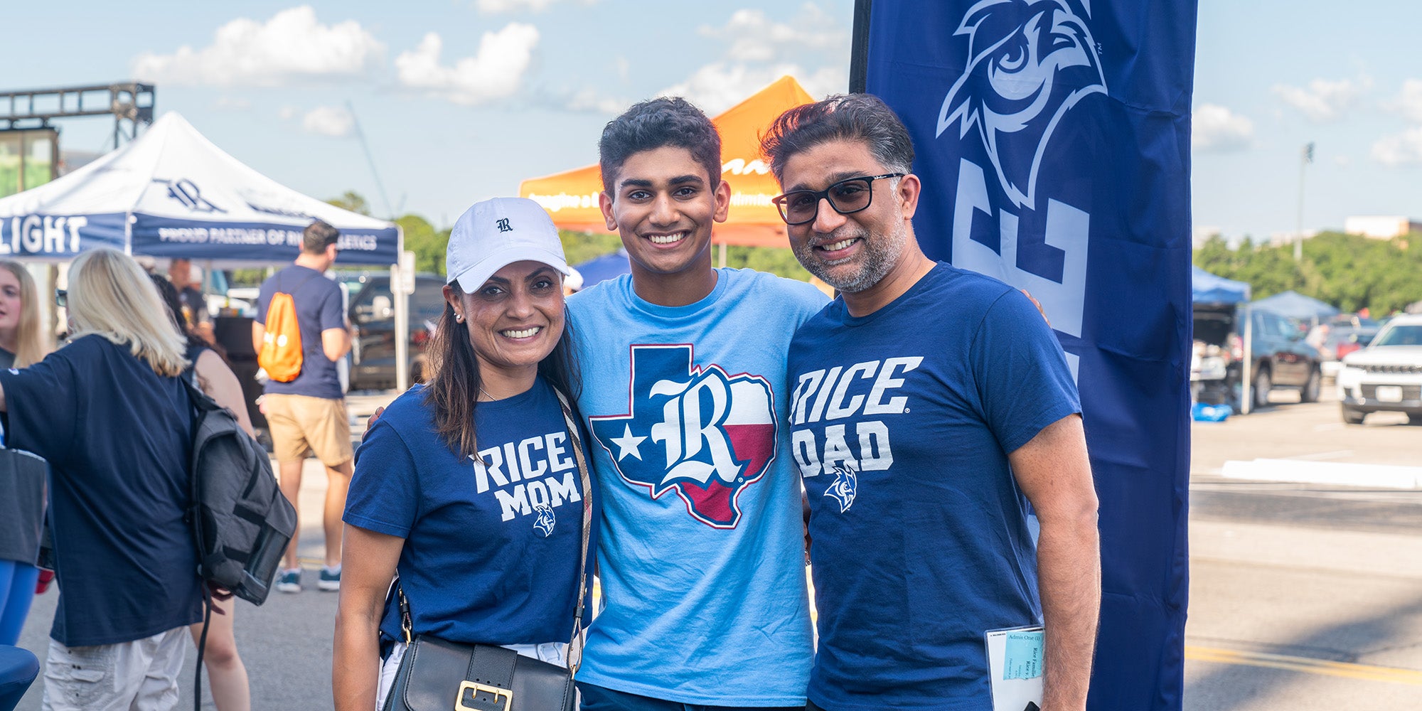 A young guy and his parents standing together in front of a parking lot and banner
