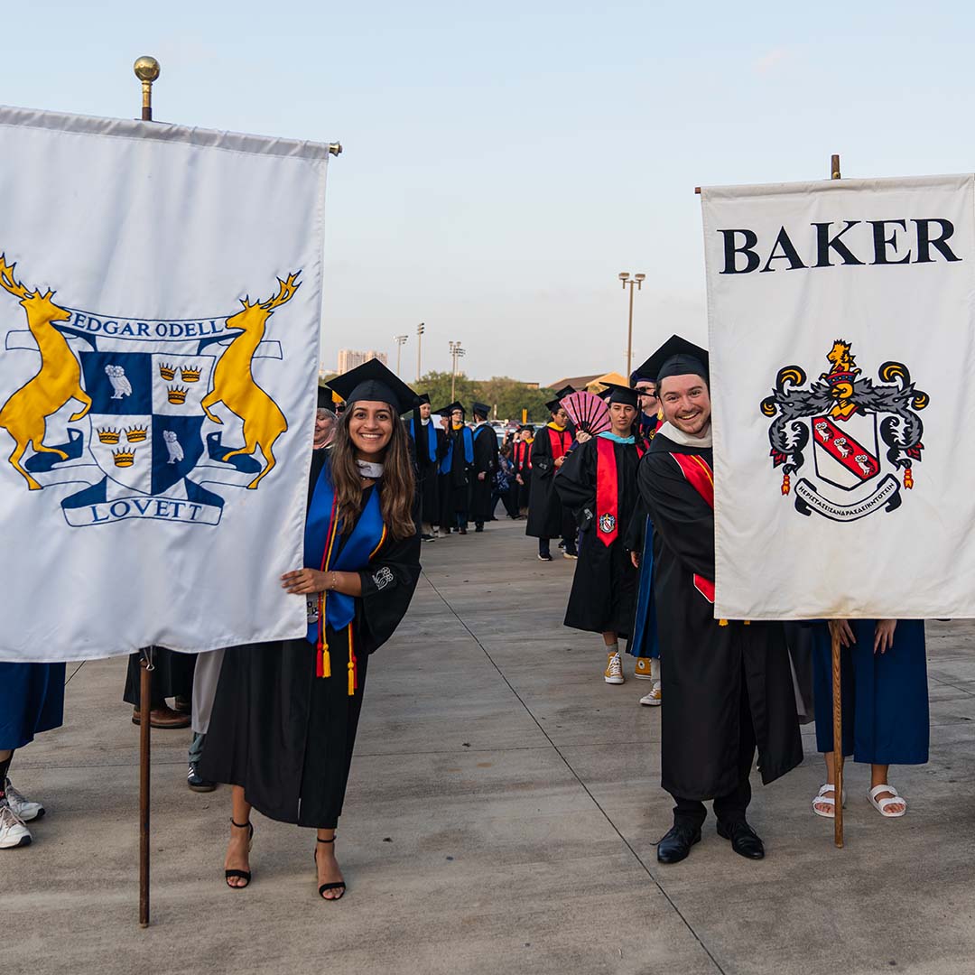 Two students smile for a picture as they hold large banners that say Lovett College and Baker College respectively.