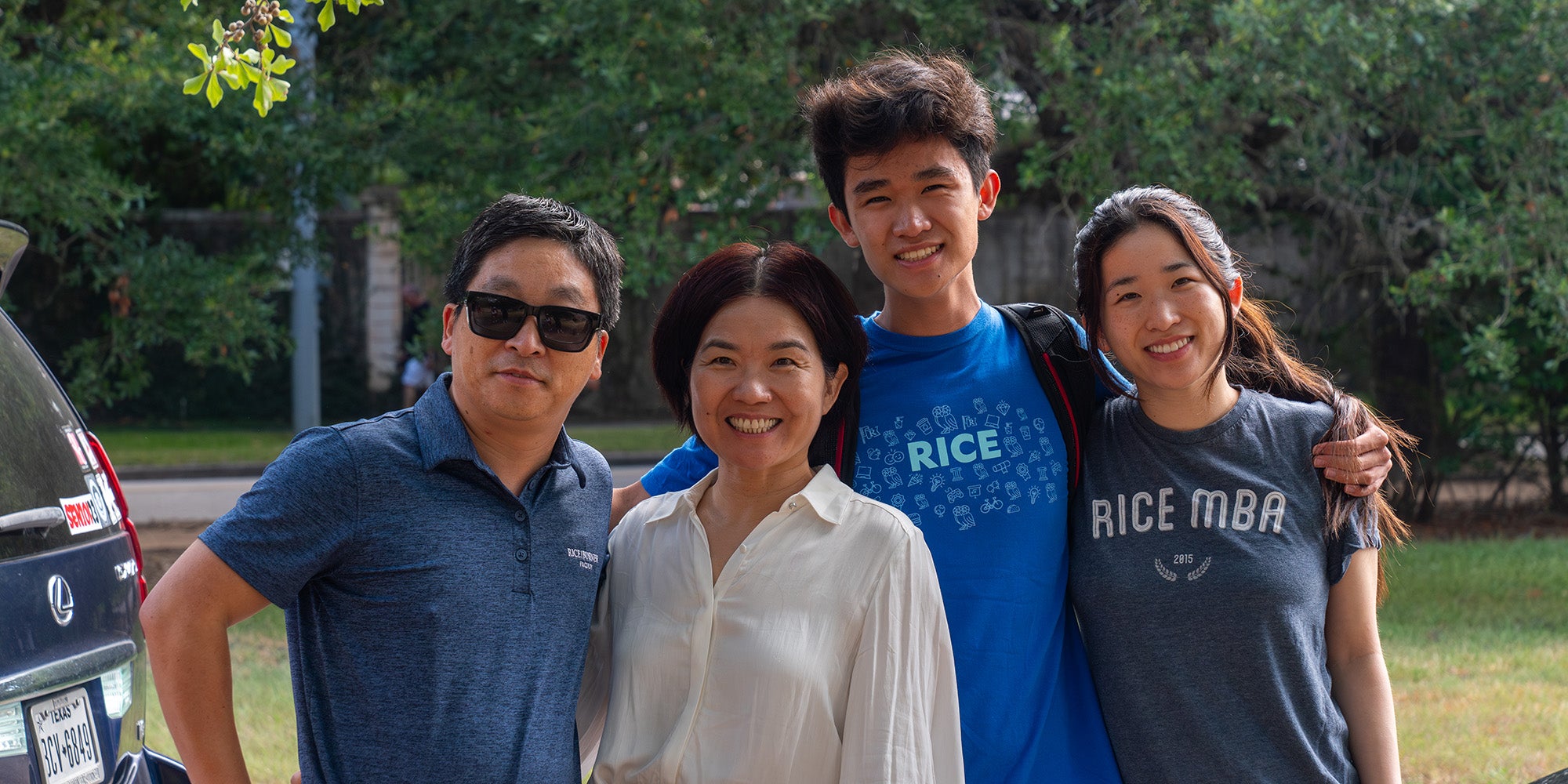 An Asian family posing together for a photo outdoors, the son and daughter wearing branded Rice University shirts
