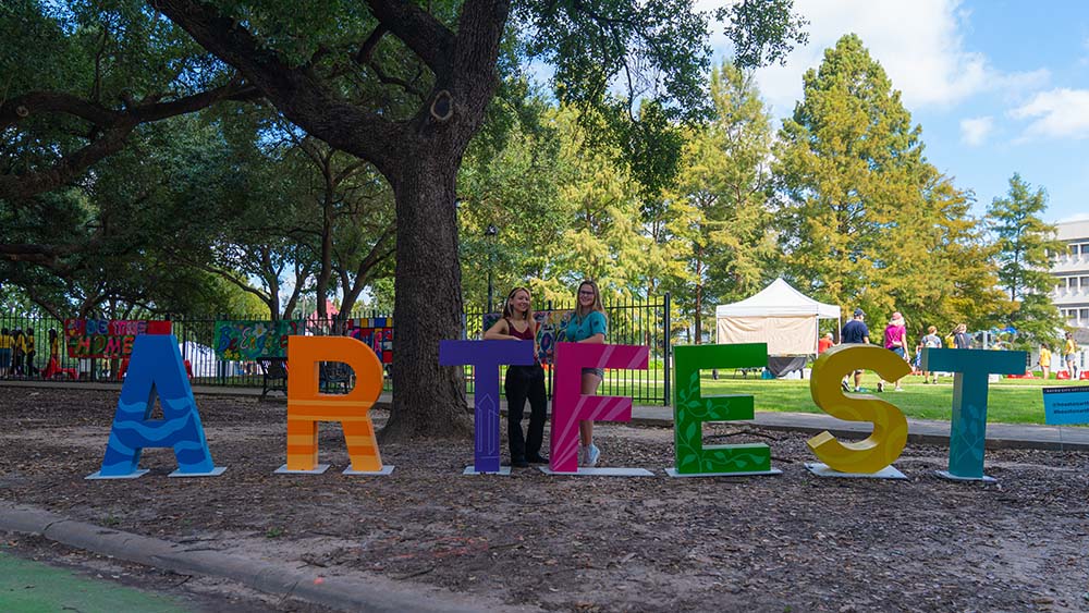 Two female Rice students stand behind life-size blocks that spell out Art Fest in different colors.