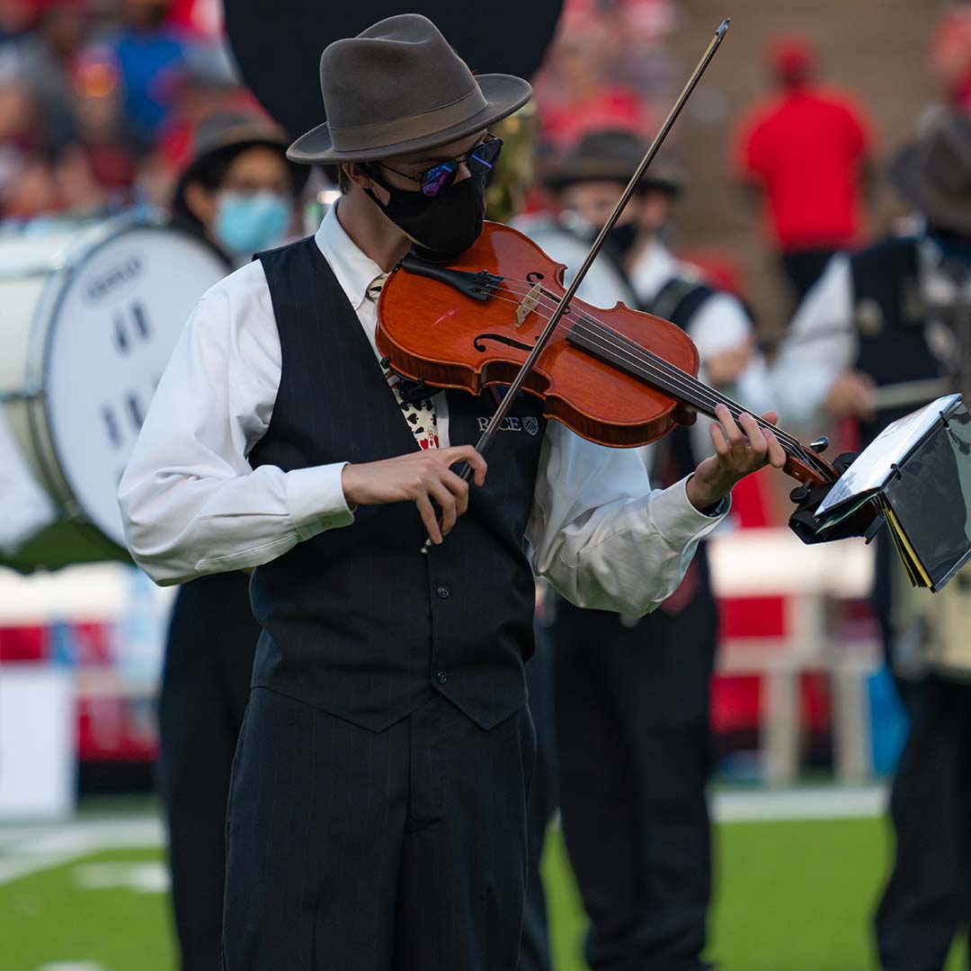 A student that's part of the Rice Marching Owl Band (MOB) plays the violin on the football field at half-time.