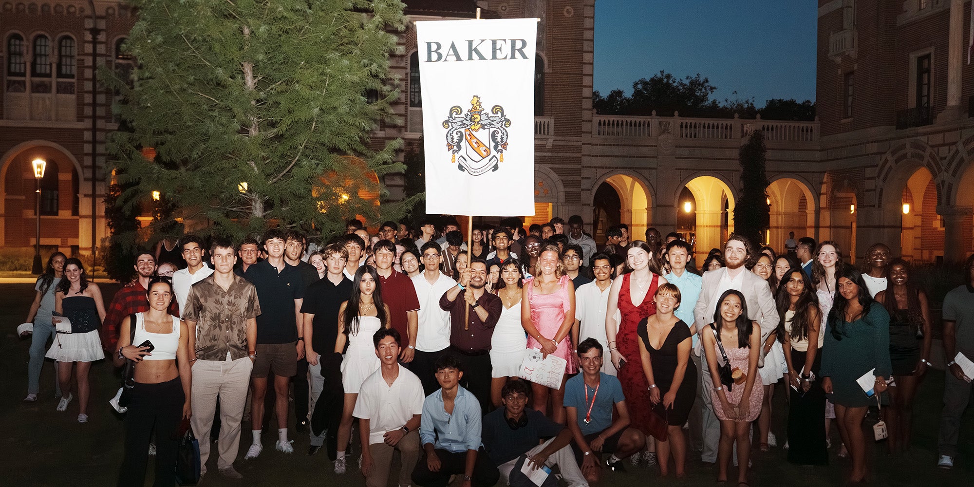 Huge crowd of people holding white flag banner sporting "BAKER" and logo on it outdoors at night