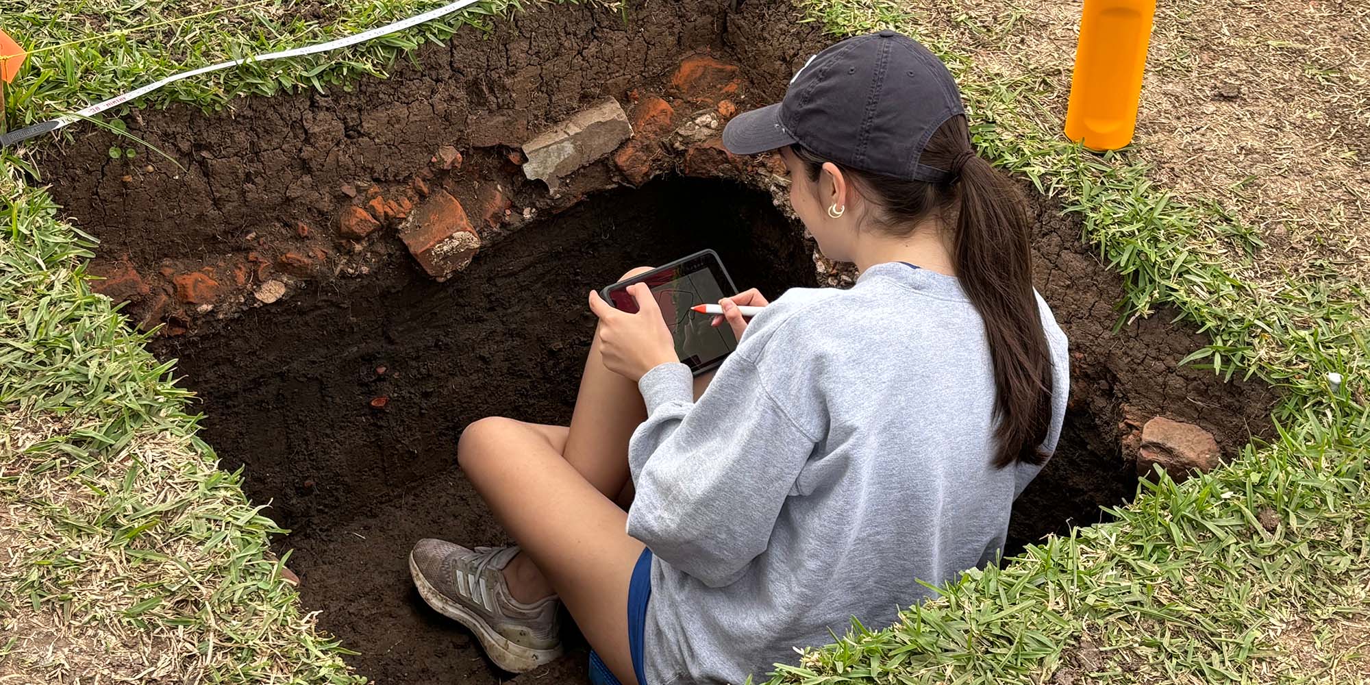 Girl sitting inside square hole dug in the grass