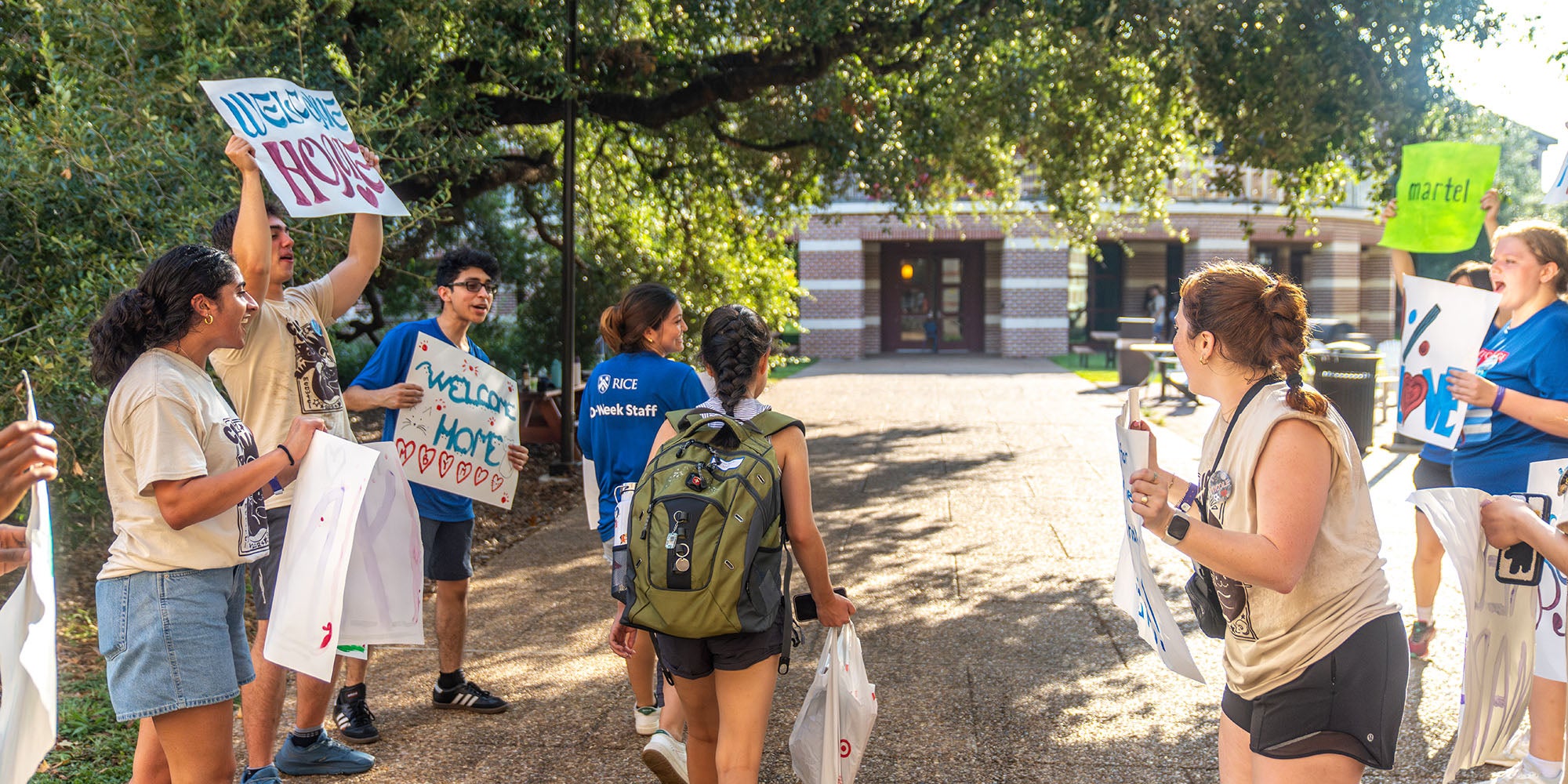 A new student follows an O-Week staff member to their residential college, flanked by students with "welcome" posters