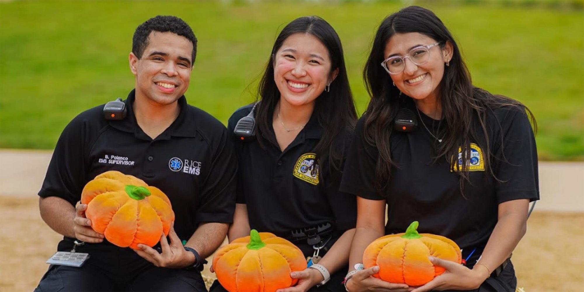 3 college students posing sitting on a hay bale and holding pumpkins