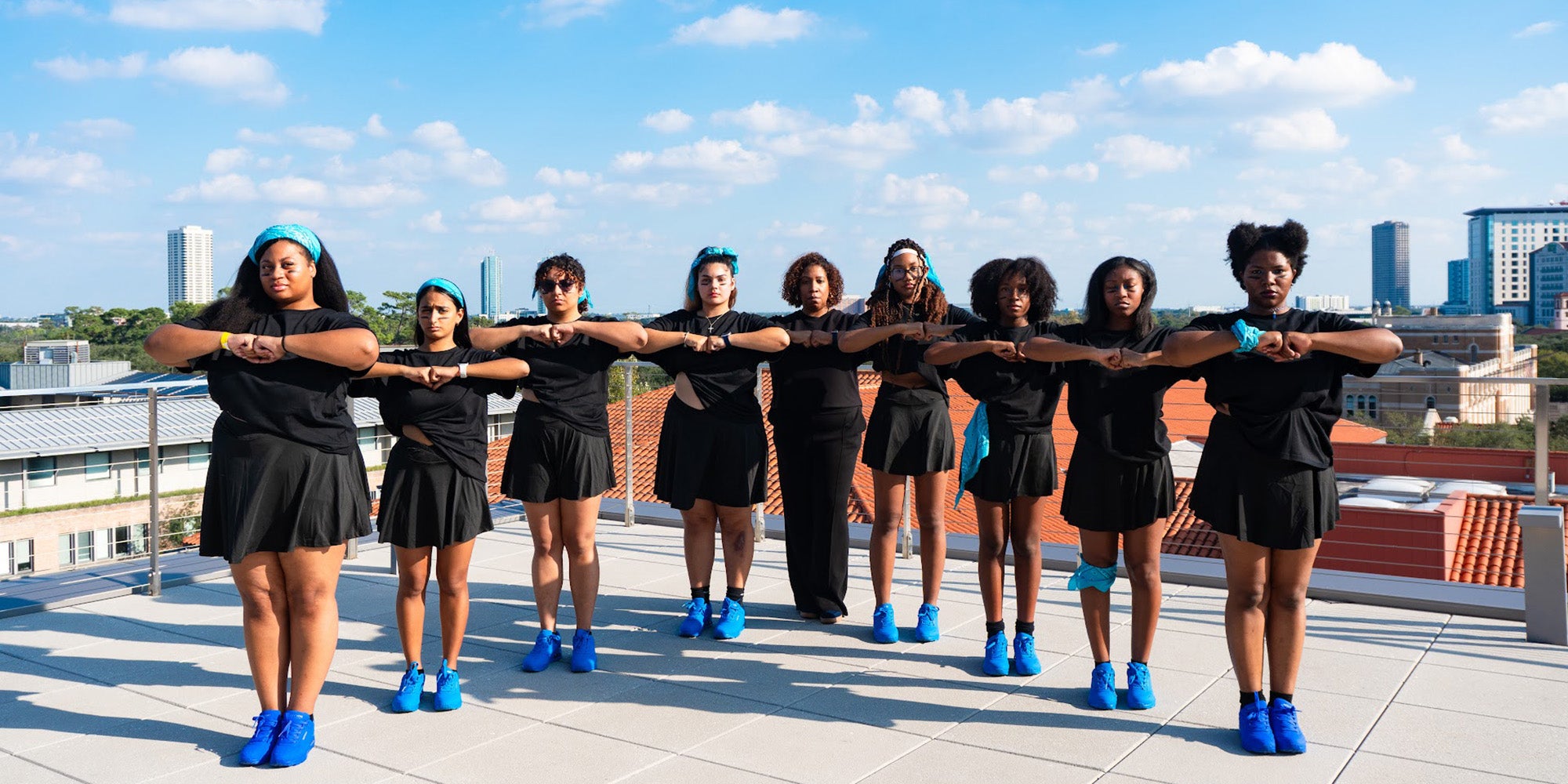 9 students in matching black clothing and blue sneakers, posed with elbows out