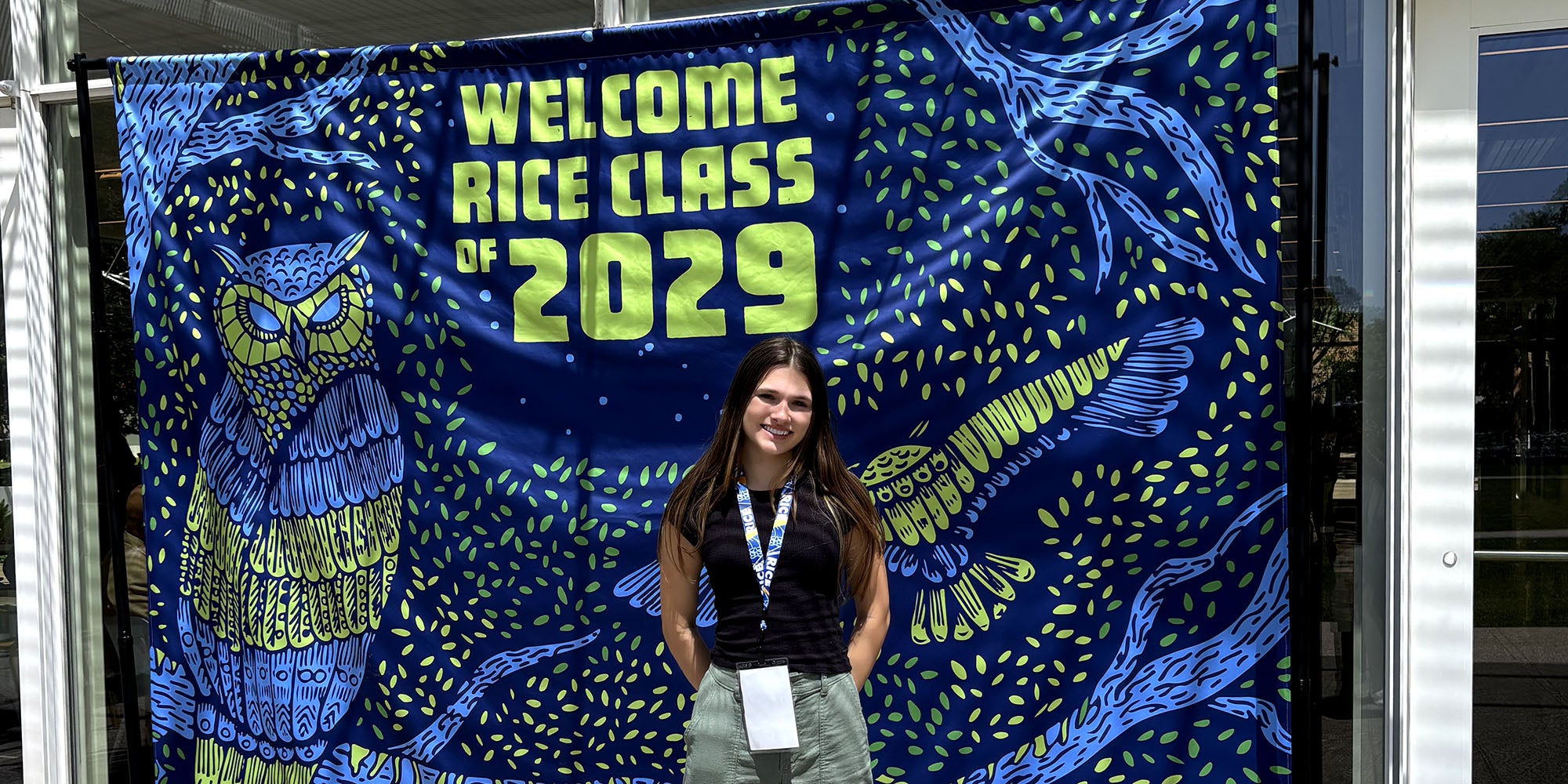 A girl standing in front of a vivid, blue banner with the text "Welcome Class of 2029"