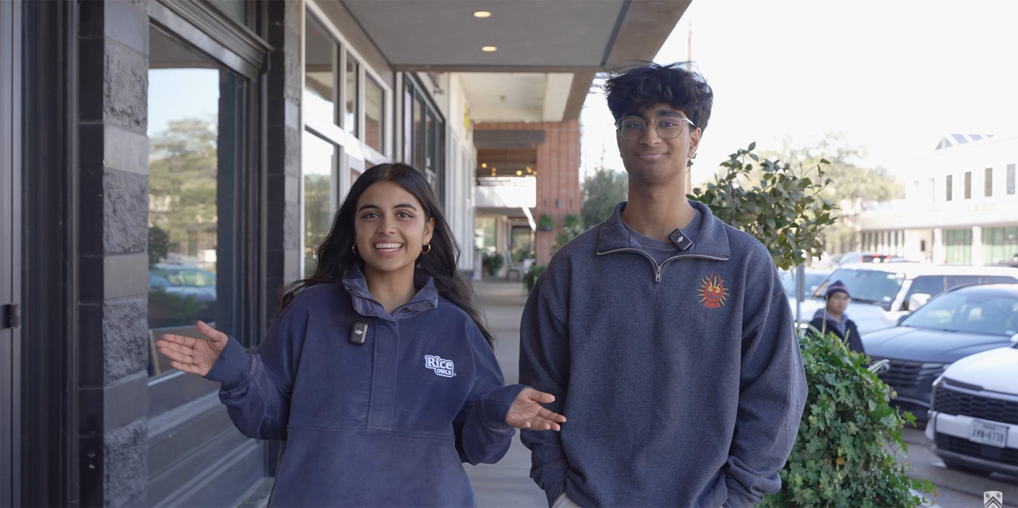 Two people smiling, gesturing on a sidewalk outside of a building