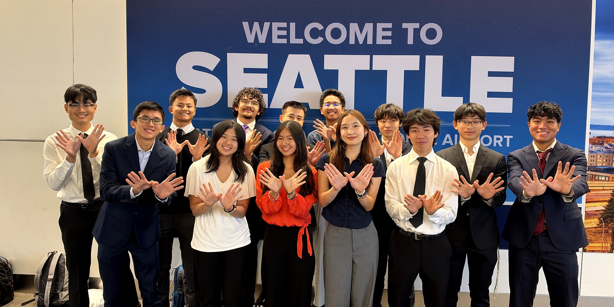 Large group of people in business formal attire standing in front of a sign that says "Welcome to Seattle" in white block letters