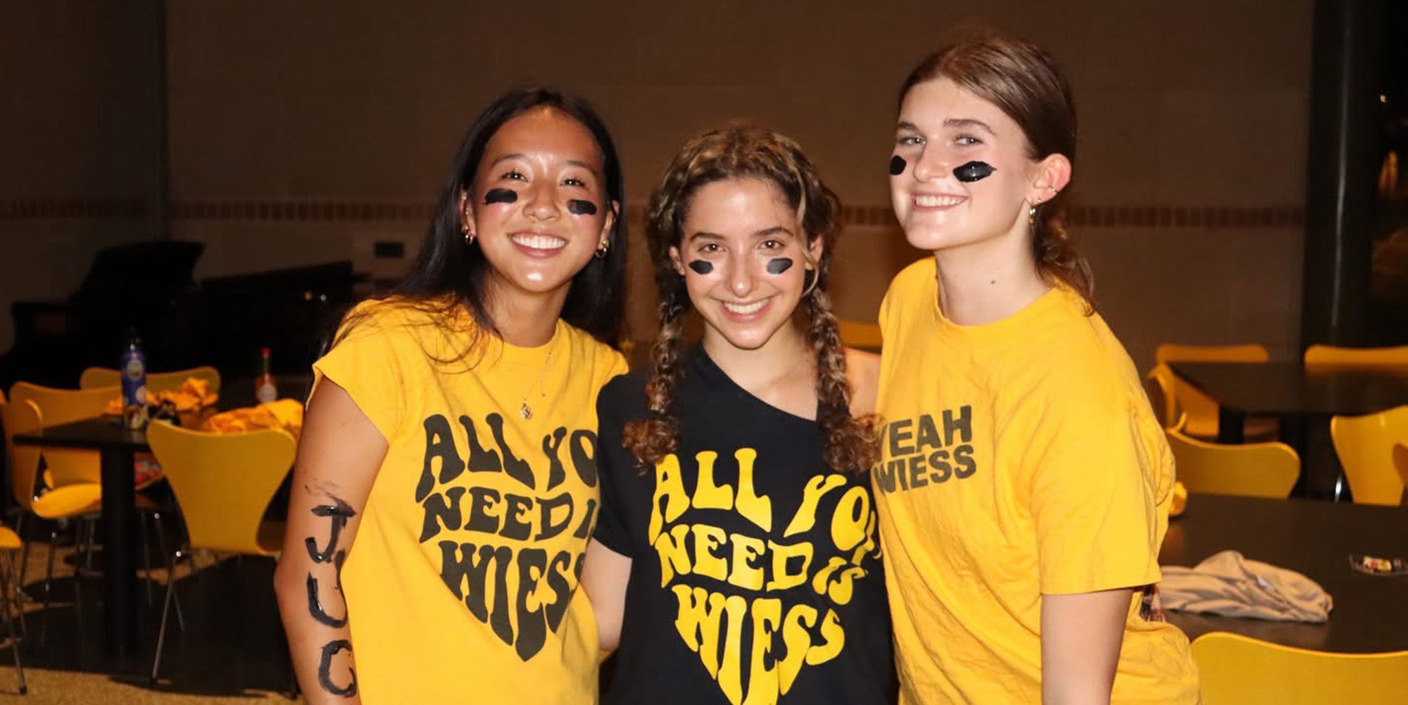 Three girls in yellow and black graphic T-shirts and face painting