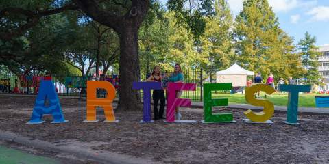 Two female Rice students stand behind life-size blocks that spell out Art Fest in different colors.