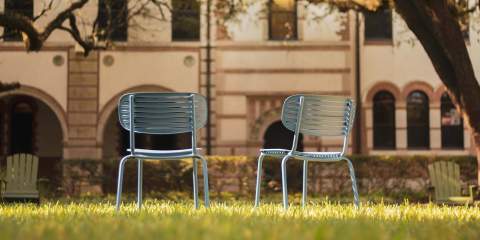 A picture of two empty metal chairs on a lawn on Rice University's campus.