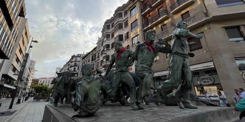 A picture of statues outdoors in a street in Spain, showing a bull charging towards four men running away.