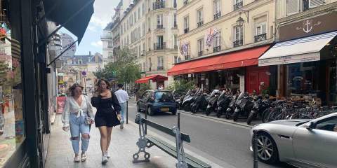 A picture of a street in Paris featuring some cafes with brightly covered awning and with lots of mopeds and bikes parked out front.