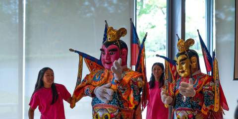Two teenage volunteers assist colorfully dressed up god and godess characters performing for the crowd.
